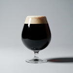 Glass of dark beer with a light head on a gray background