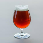 Glass of amber liquid with a head of foam on a gray background