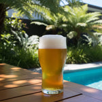 Glass of beer on a wooden table by a pool with greenery in the background