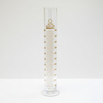 Clear glass measuring cylinder with gold markings on a white background