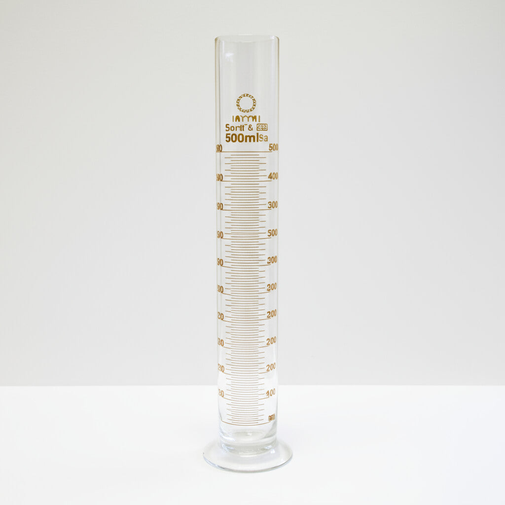 Clear glass measuring cylinder with gold markings on a white background